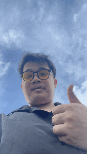 a man wearing glasses and giving a thumbs up