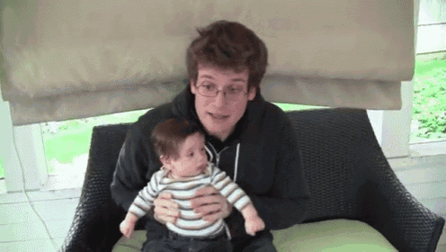 a man is holding a baby in his arms while sitting on a chair .