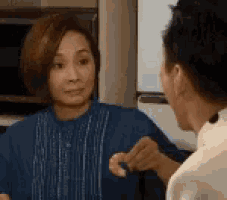 a man and a woman are talking to each other in a kitchen . the woman is holding something in her hand .
