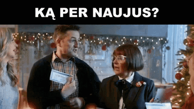 a man and a woman are standing next to each other in front of a christmas tree and a sign that says ka per naujas