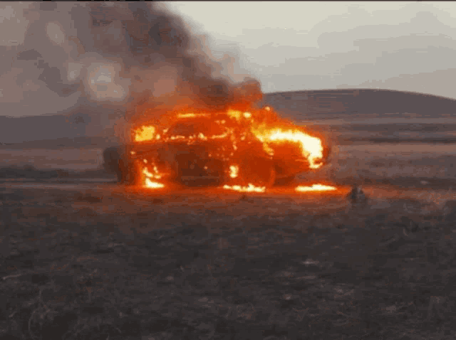 a car is on fire in a field with smoke coming out of it