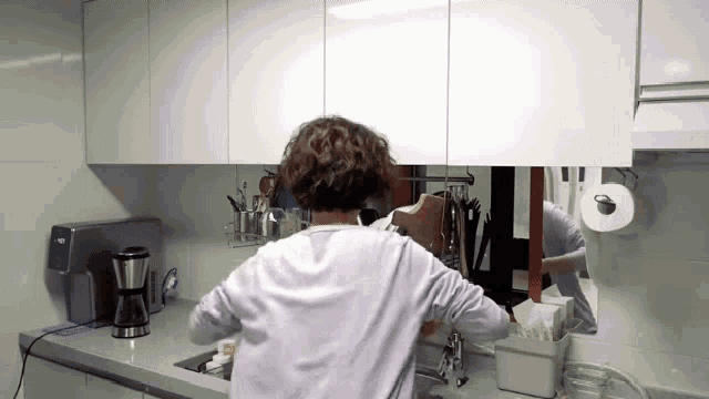 a woman is washing dishes in a kitchen and looking at herself in the mirror .