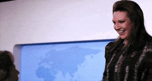a woman is smiling in front of a map of the world in a room .
