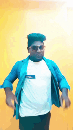 a man wearing sunglasses and a blue shirt is dancing in front of a yellow wall .
