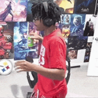 a man wearing headphones and a red shirt is standing in front of a wall with posters .