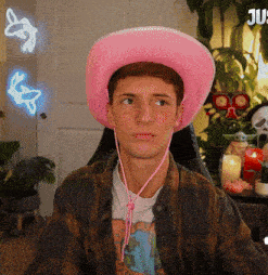 a young man wearing a pink cowboy hat and a plaid shirt looks at the camera