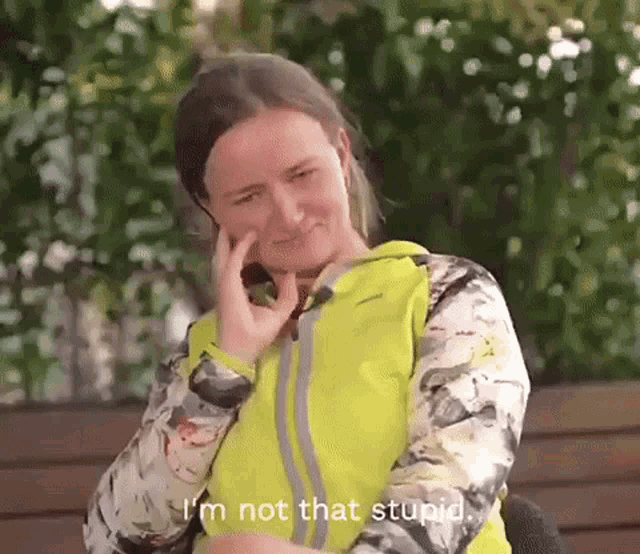 a woman in a yellow jacket is talking on a cell phone and says " i 'm not that stupid " .