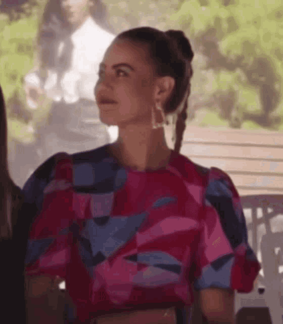 a woman in a pink and blue dress is sitting on a bench with other people .