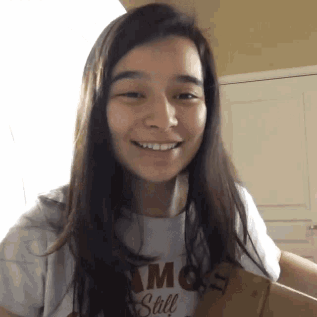 a woman wearing a shirt that says " am still " smiles while holding a cardboard box