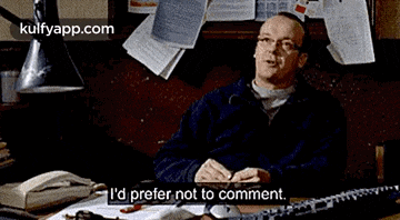 two men in suits and ties are standing next to each other in an office and one of them is talking to the other .