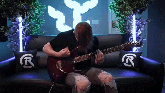 a man playing a guitar on a couch with pillows that say r