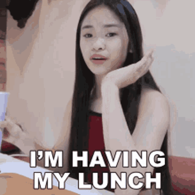 a woman is sitting at a table with a cup of coffee and says i 'm having my lunch