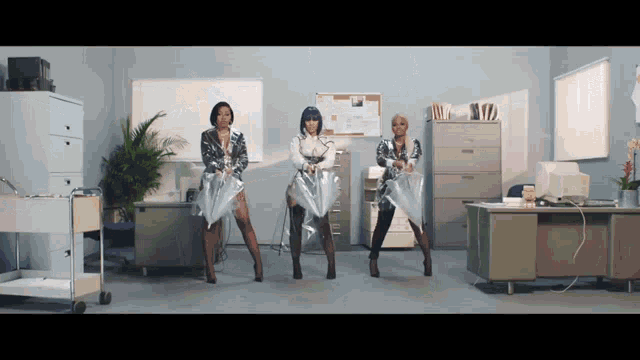 a group of women are dancing in an office with plastic umbrellas