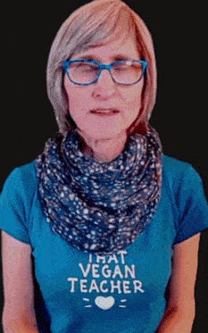 a woman wearing glasses and a scarf is wearing a t-shirt that says that vegan teacher