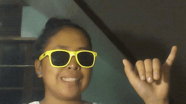 a girl wearing a pair of yellow sunglasses making a shaka sign