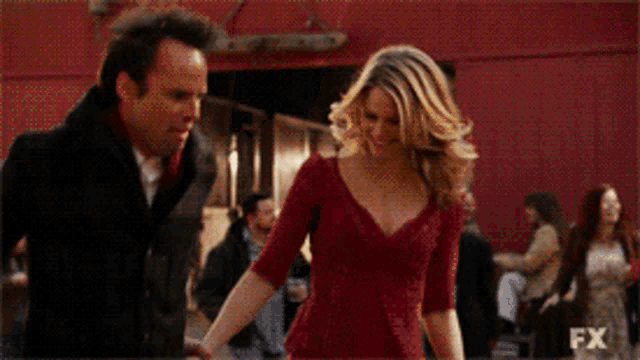 a woman in a red dress holds hands with a man in a black coat with fx written on the bottom