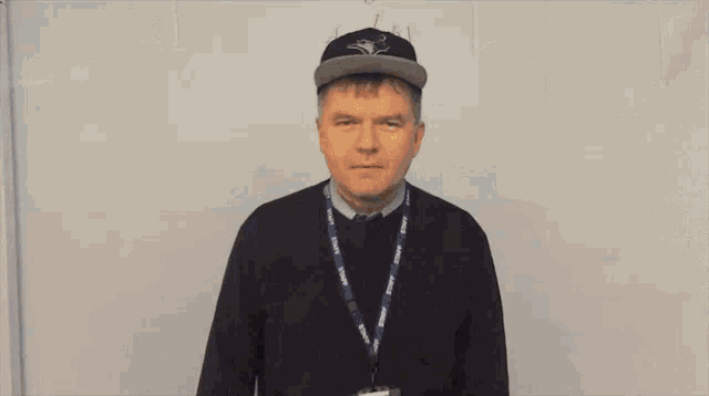 a man wearing a hat and a lanyard is standing in front of a white board with a math problem on it .