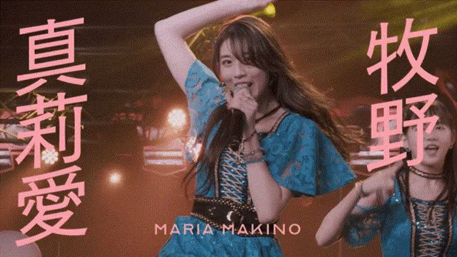 a woman in a blue dress singing into a microphone with maria makino on the bottom