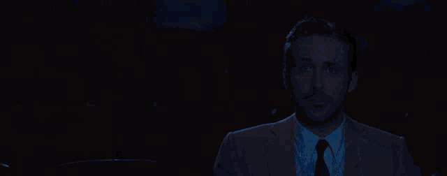 a man in a suit and tie is standing in front of a projector screen in a dark room .
