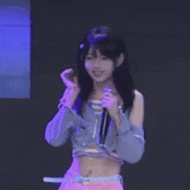 a girl in a crop top is holding a microphone in her hand .