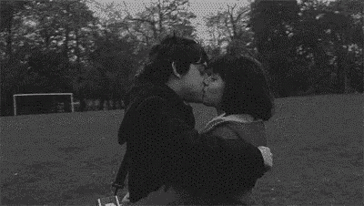 a man and a woman are kissing in a park .