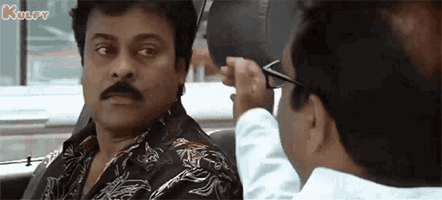 a man with a mustache and glasses is sitting in a car with another man .