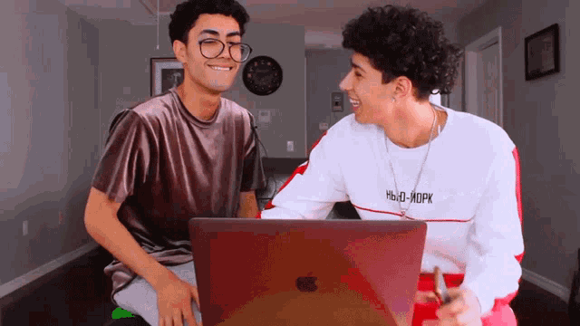 two young men are looking at a laptop and one has a shirt that says hello-mork on it