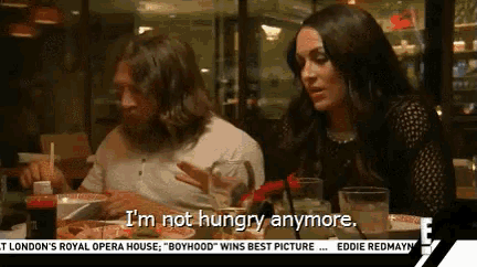 a man and a woman are sitting at a table and the woman is saying i 'm not hungry anymore