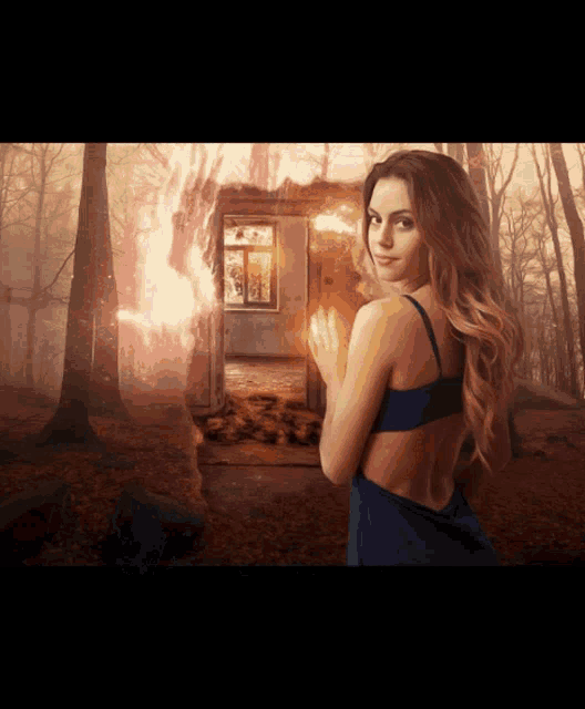 a woman in a blue dress stands in front of a burning house