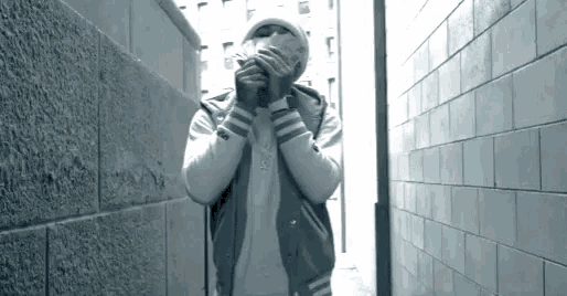 a man wearing a mask and a varsity jacket is standing in a narrow alleyway