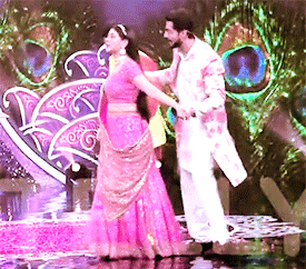 a man and a woman are dancing on a stage with peacock feathers behind them