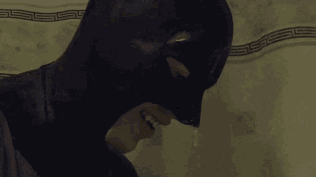a man in a batman costume is standing in front of a wall with a greek key pattern