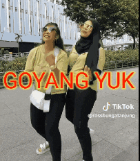 two women are standing next to each other on a sidewalk with the words goyang yuk written in red