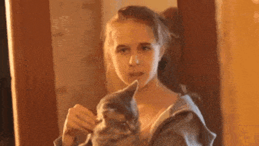 a young girl is holding a cat in her arms and looking at it in a mirror .