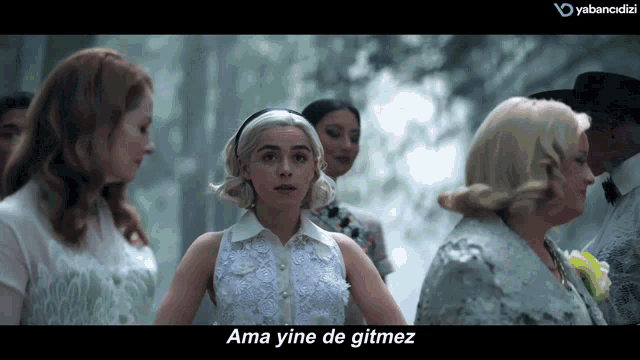 a woman in a white dress stands in front of a group of women and says ama yine de gitmez