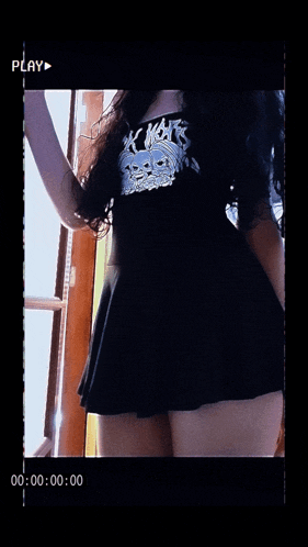 a woman in a black dress is standing in front of a window with a play button on the bottom