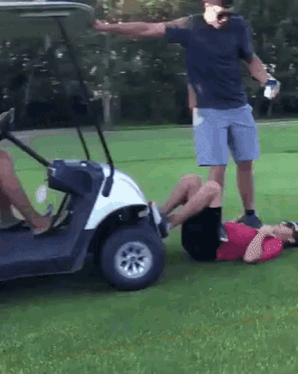 a man standing next to a golf cart with a woman laying on the ground in front of it