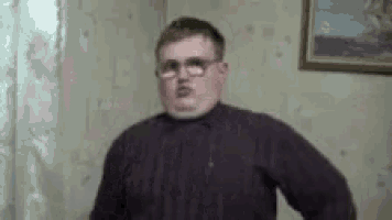 a man wearing glasses and a purple sweater is standing in a room with a picture on the wall .
