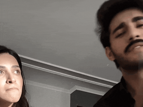 a man with a mustache looks at a woman who is making a funny face