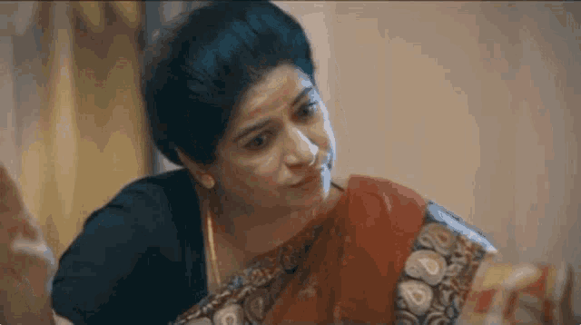 a woman in a red saree is sitting on a bed and looking at something .
