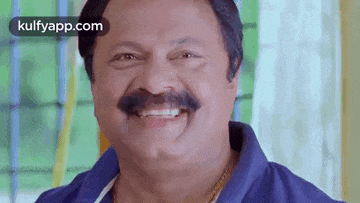 a man with a mustache is smiling while wearing a blue shirt .