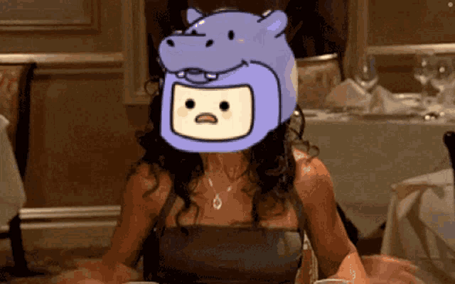 a woman sitting at a table with a purple hippo hat on her head