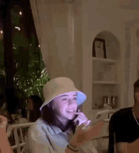 a woman wearing a bucket hat is sitting at a table in a room .