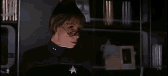 a woman wearing glasses and a star trek uniform is looking at the camera in a dark room .