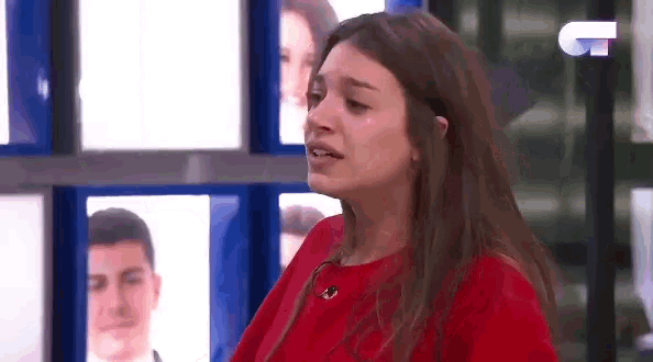 a woman in a red shirt is crying while standing in front of a wall of pictures .