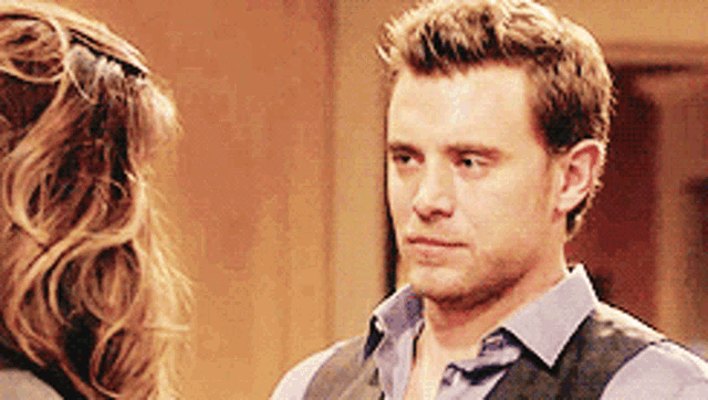 a man wearing a vest and a blue shirt is looking at a woman