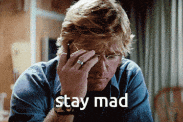 a man wearing glasses is talking on a cell phone and the words stay mad are displayed above him