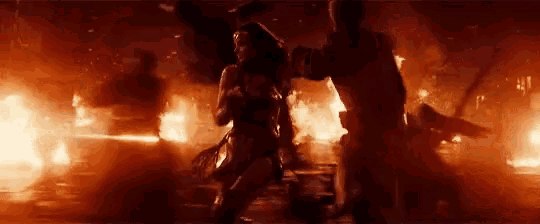 a woman in a wonder woman costume is standing in front of a burning building .