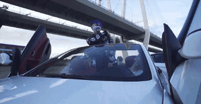 a man wearing a purple hat and a mask stands next to a car with the door open