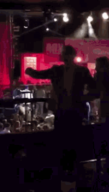 a group of people are dancing in a dark room with a red curtain in the background .